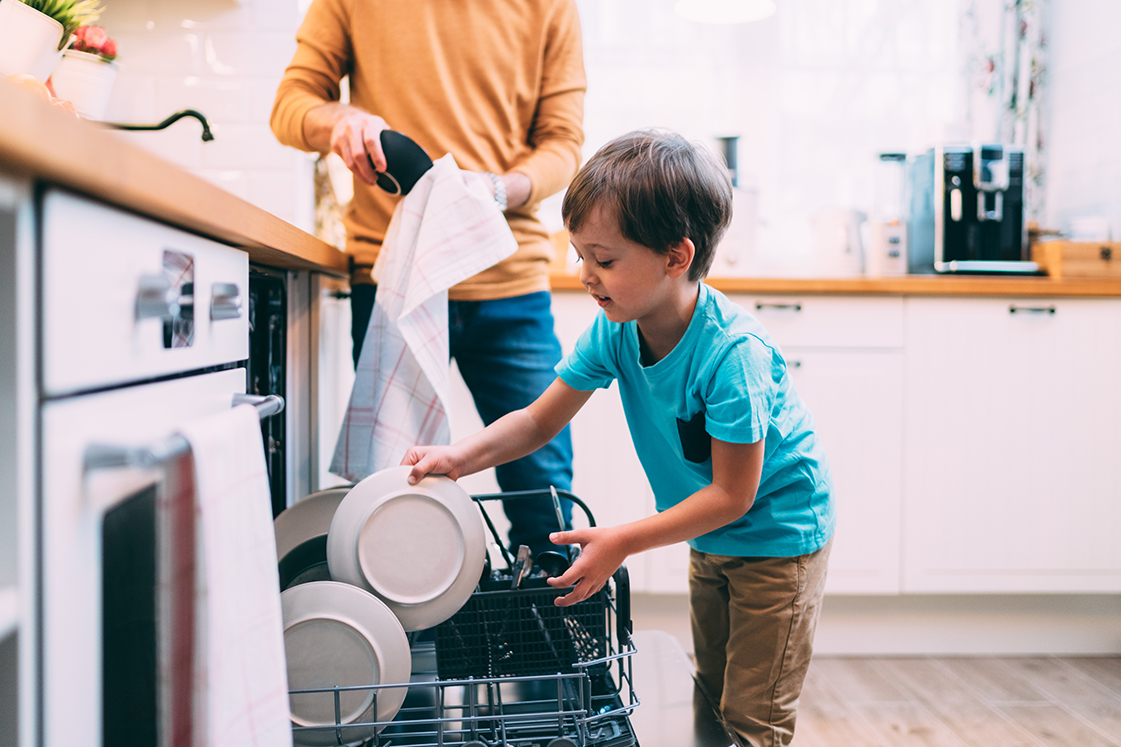 A young boy helps his father load the dishwasher